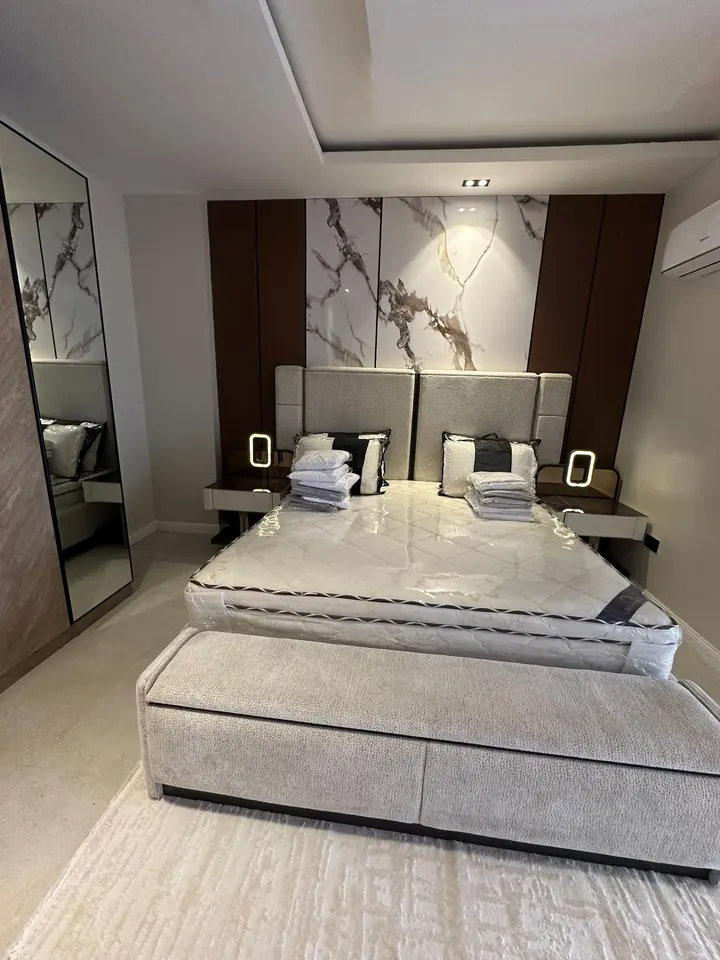 Bedroom with a marble-look feature wall, timber panels and a tray ceiling with recessed lights