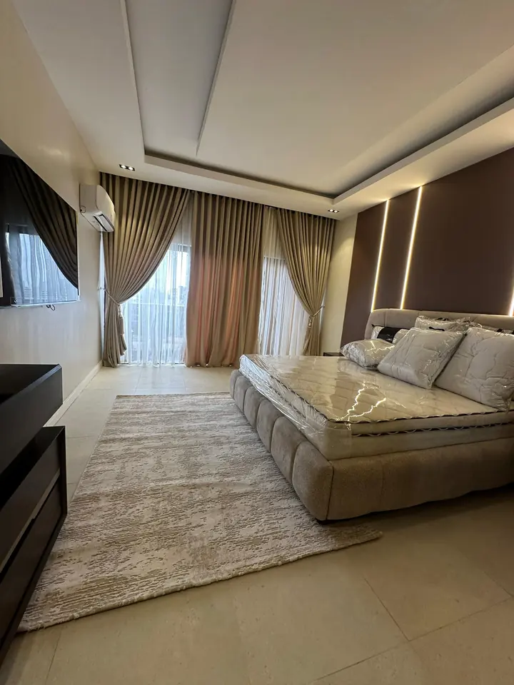 Bedroom with a tray ceiling, LED strip lighting beside the headboard wall and floor-length curtains