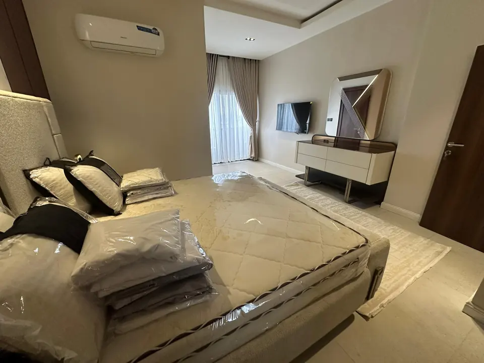 Bedroom with an upholstered bed, wall-mounted TV, curtains and recessed ceiling lights