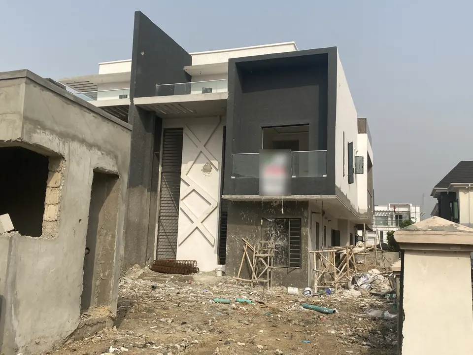 House frontage with dark and white render, a glass balcony and boundary wall work still in progress